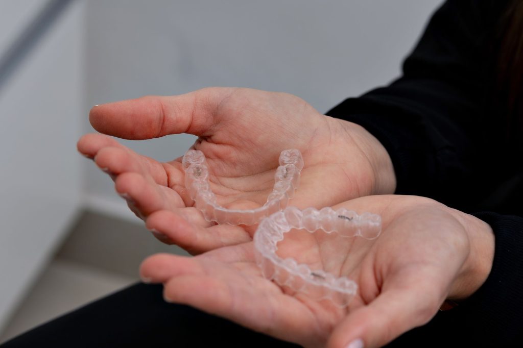 Two clear aligner trays held in open hands