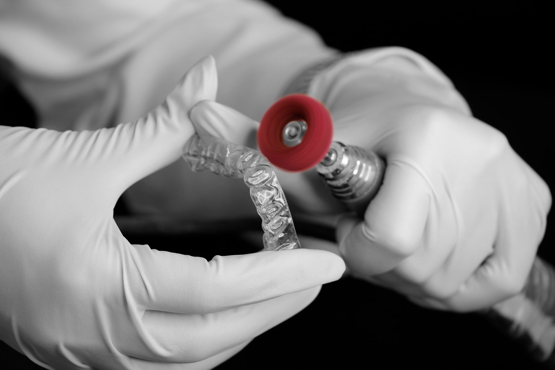 Gloved hands polishing the edge of a clear aligner with a dental lab tool