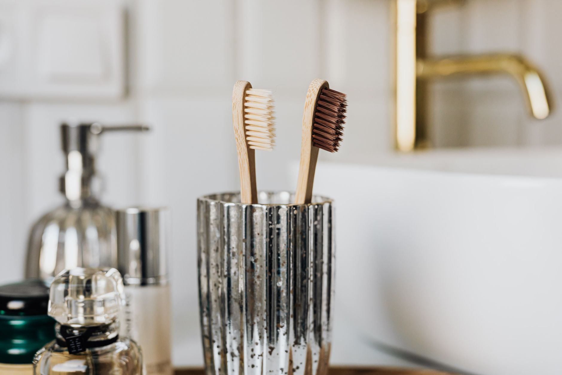 Two bamboo toothbrushes in a glass beside a bathroom basin